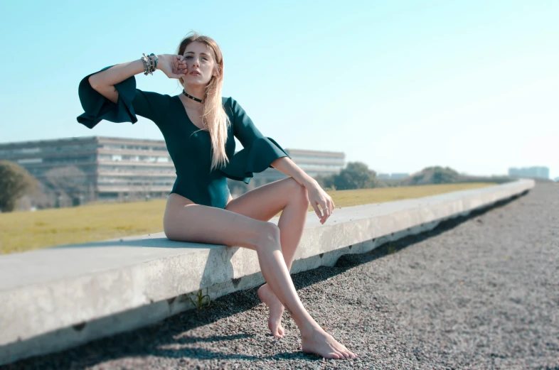 a woman sitting on top of a cement bench, inspired by Elsa Bleda, pexels contest winner, green swimsuit, fashion pose, blue sky, long thin legs