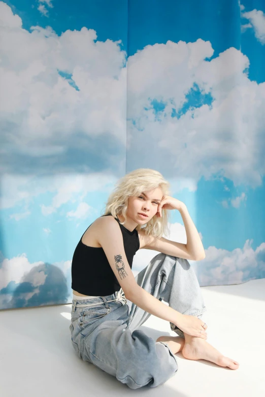 a woman sitting on top of a white floor, an album cover, inspired by Elsa Bleda, trending on pexels, tattoos of cumulus clouds, dressed anya taylor - joy, studio backdrop, jeans and t shirt