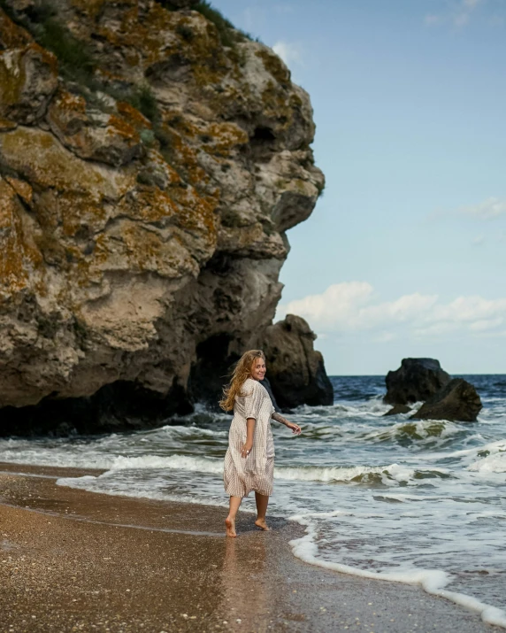 a woman walking on a beach next to the ocean, inspired by Pierre Puvis de Chavannes, pexels contest winner, renaissance, standing in a grotto, ukraine. photography, non-binary, beautiful nordic woman