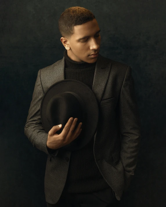 a man in a suit holding a hat, an album cover, inspired by Randy Vargas, black and brown, lgbtq, proud looking away, dark. no text