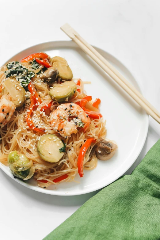 a white plate topped with noodles and vegetables, chopsticks, food, shrimp, jen yoon