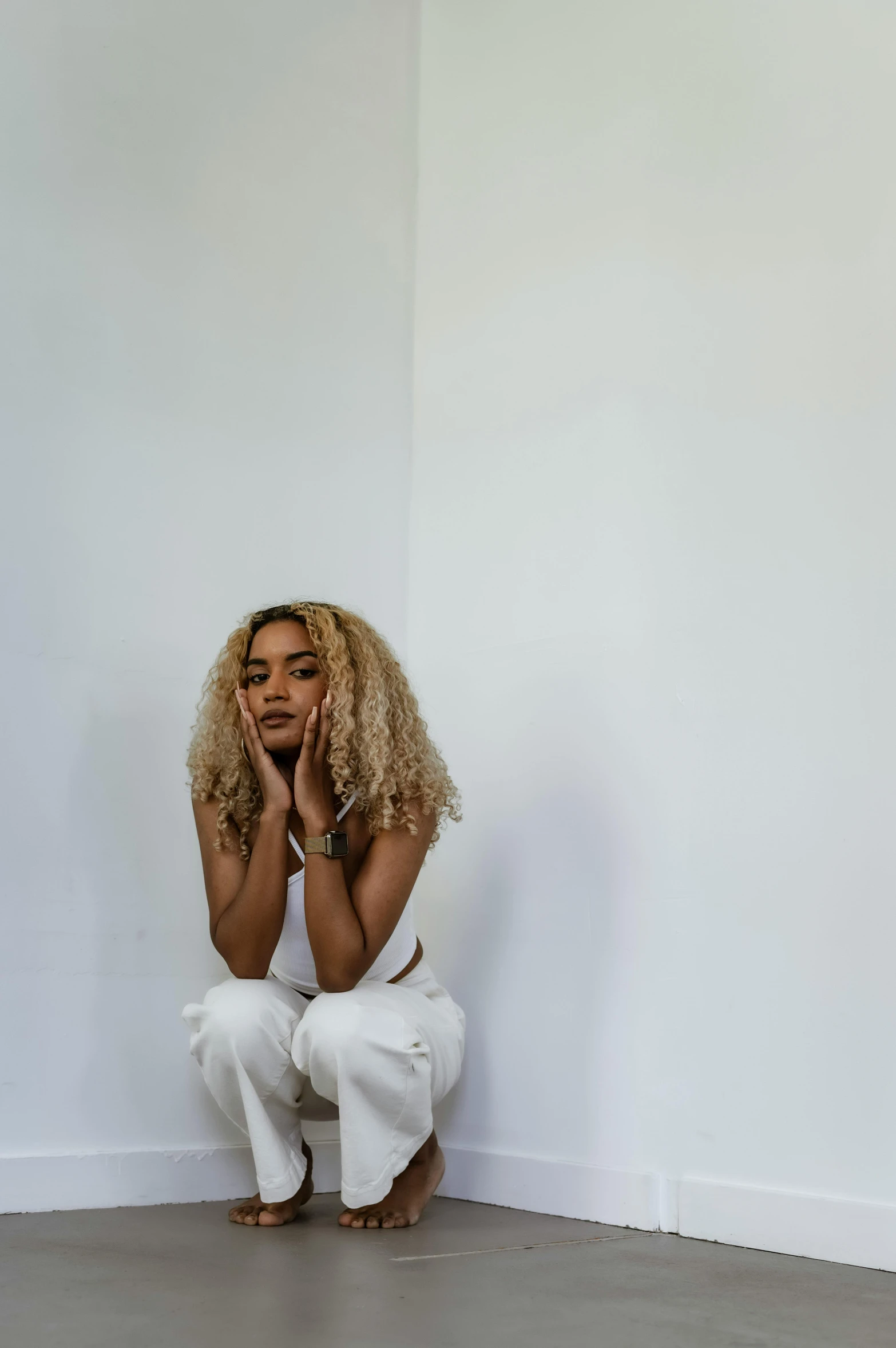 a woman sitting on the floor in a white room, by Sophia Beale, trending on pexels, short blonde afro, ashteroth, distraught, white pants