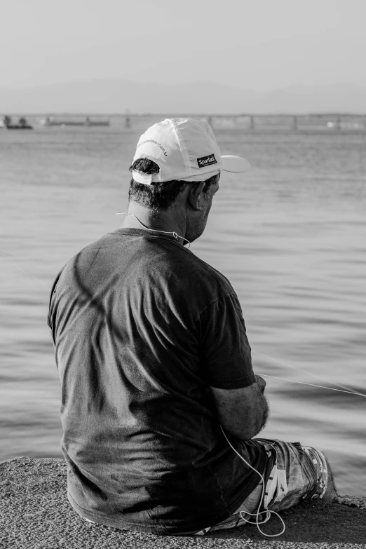 a man sitting on a rock next to a body of water, a black and white photo, by Altichiero, pexels contest winner, precisionism, wearing a baseball cap backwards, fish man, profile picture 1024px, sport