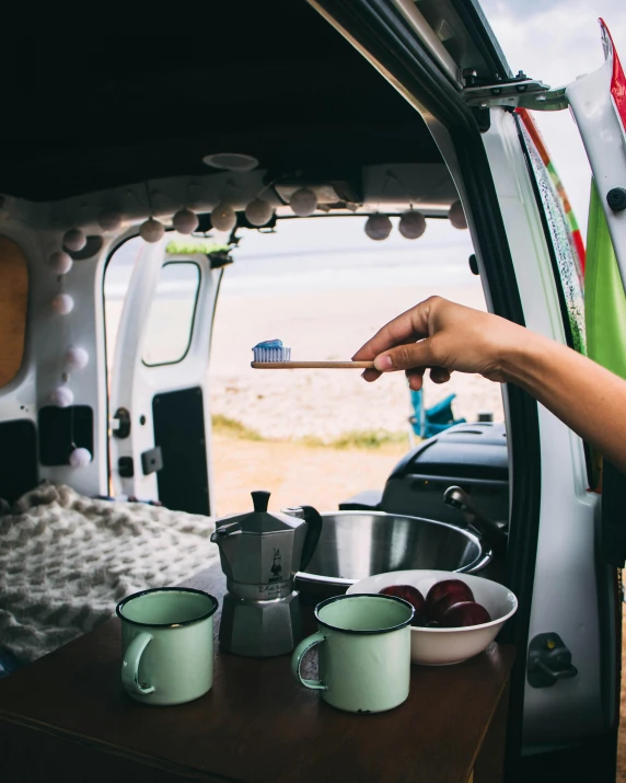 a woman is cooking in the back of a van, a picture, by Jessie Algie, trending on unsplash, square, tea, beaching, high quality photo