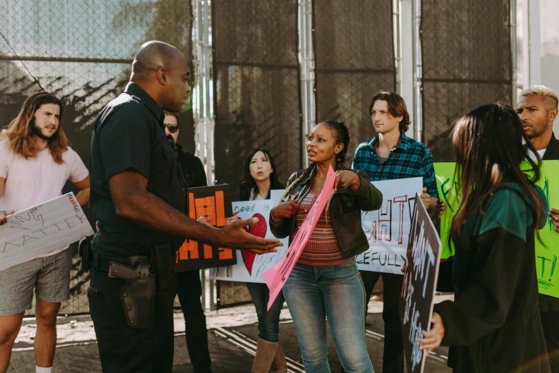 a group of people holding signs in front of a fence, by Jennifer Bartlett, pexels contest winner, black arts movement, police officers, woman holding another woman, hollywood movie still, z nation