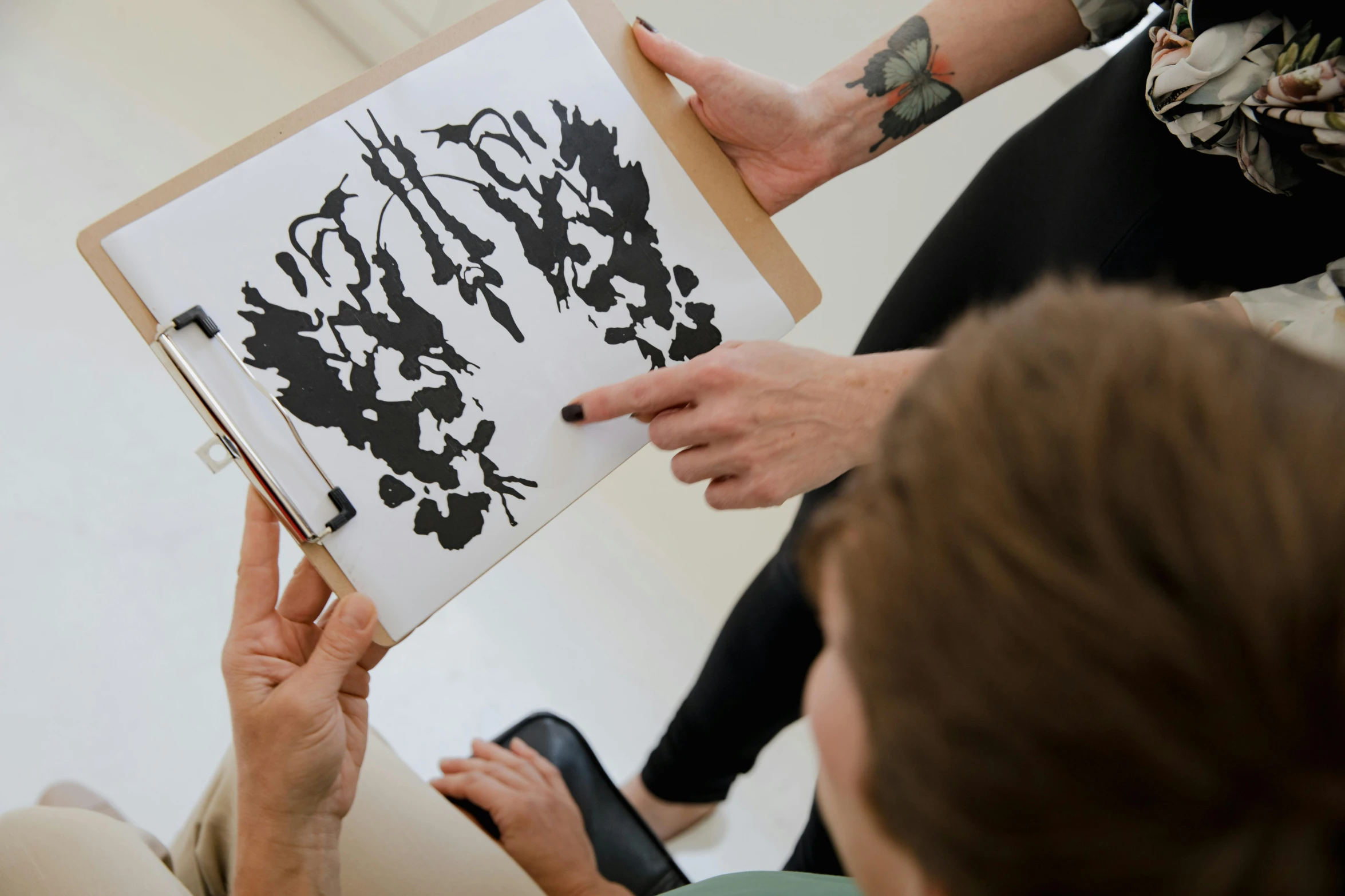 a woman holding a piece of paper with a drawing on it, by Caroline Mytinger, pexels contest winner, modern european ink painting, rorschach test, botanical anatomy, black stencil, person in foreground