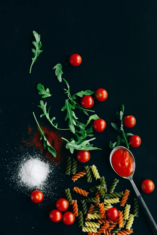 a table topped with pasta and tomatoes next to a spoon, pexels contest winner, process art, vegetable foliage, black backdrop, ketchup, on clear background