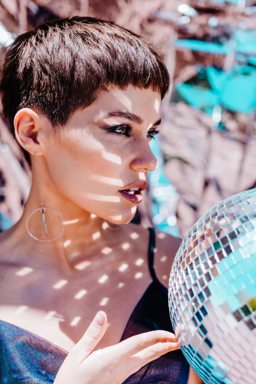 a woman holding a disco ball in front of her face, an album cover, by Julia Pishtar, trending on pexels, short black pixie undercut hair, sun - drenched, profile image, 5 0 0 px models