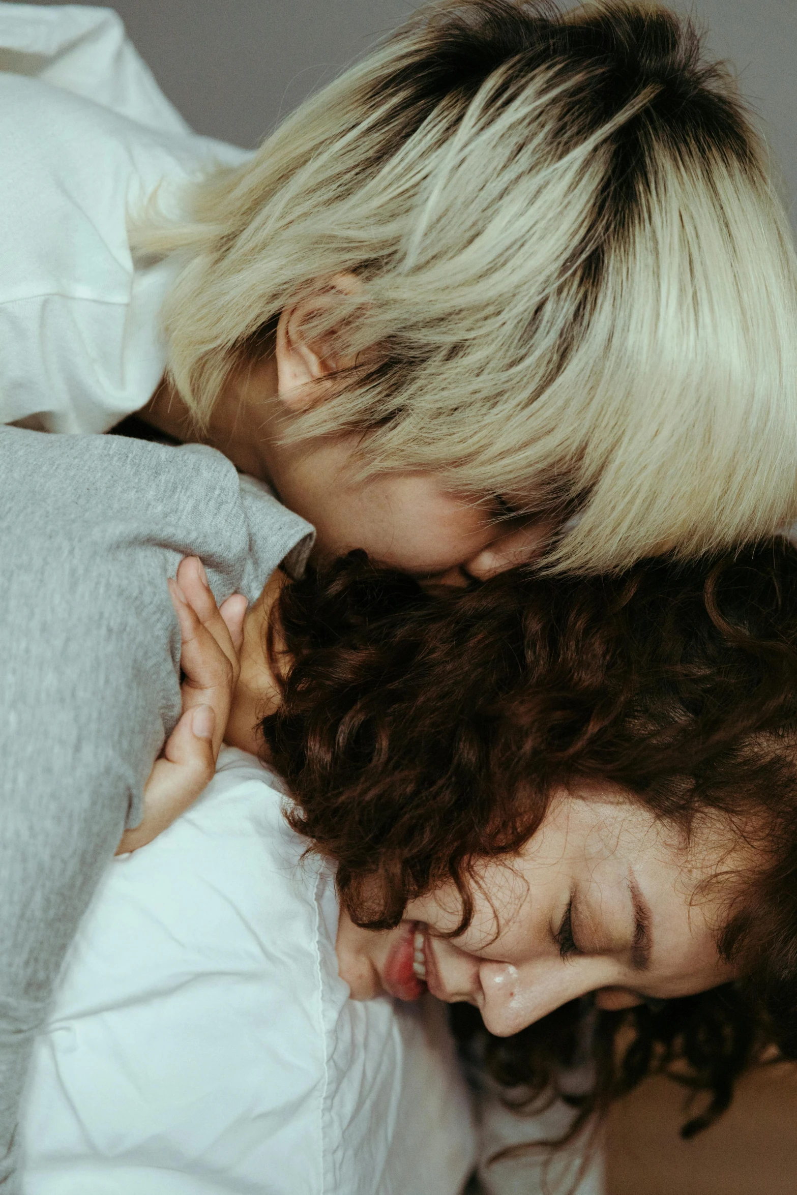 a couple of women laying on top of a bed, trending on pexels, white curly hair, hugging each other, kim hyun joo, kids