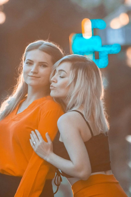 a couple of women standing next to each other, trending on pexels, happening, orange glow, lesbian embrace, blonde, hollywood promotional image