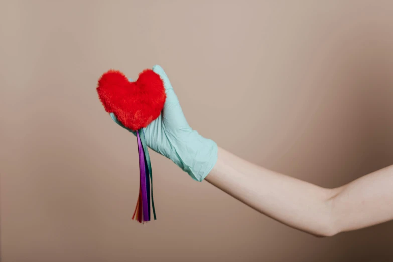 a person in blue gloves holding a red heart, inspired by Méret Oppenheim, trending on pexels, magic realism, tassels, colorful medical equipment, plush toy, roygbiv