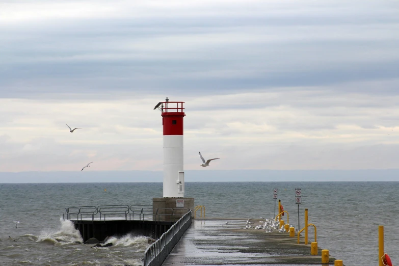 a red and white lighthouse sitting on top of a pier, by Robert Storm Petersen, pexels contest winner, birds flying in the distance, from wheaton illinois, gray, brightly lit