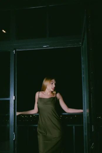 a woman standing in front of a glass door, inspired by Elsa Bleda, unsplash, rooftop party, dark green dress, low quality photo, gif
