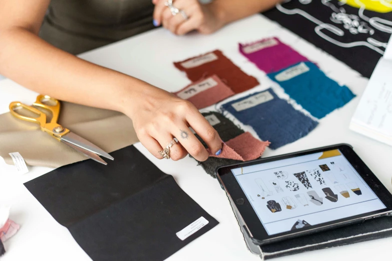 a woman sitting at a table using a tablet computer, by Nicolette Macnamara, trending on pexels, arbeitsrat für kunst, fabrics textiles, leather clothes, 9 9 designs, medium close up