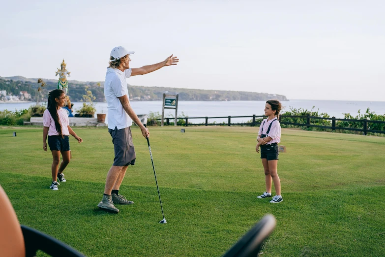 a man standing on top of a lush green field, clubs, kids playing, manly, golf course