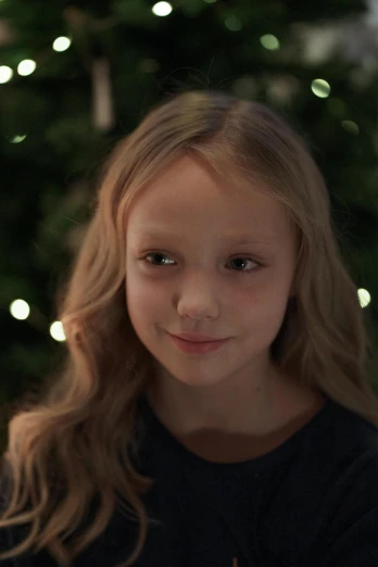 a little girl sitting in front of a christmas tree, by David Donaldson, pexels contest winner, video art, annasophia robb, lovingly looking at camera, portrait sophie mudd, medium close up