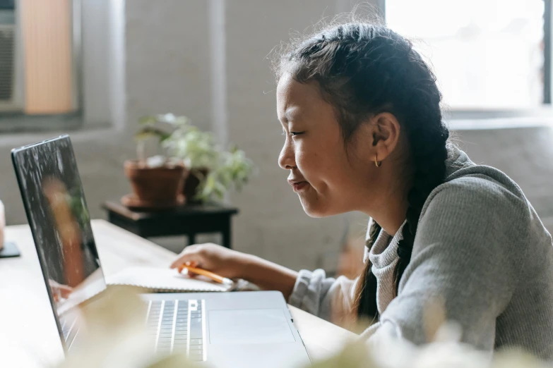 a woman sitting in front of a laptop computer, by Nicolette Macnamara, pexels contest winner, young asian girl, working on a laptop at a desk, profile image, aged 13