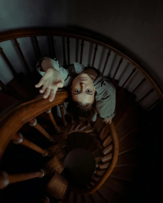 a woman standing on top of a wooden spiral staircase, inspired by Elsa Bleda, pexels contest winner, tired haunted expression, smiling down from above, from horror movies, hands straight down