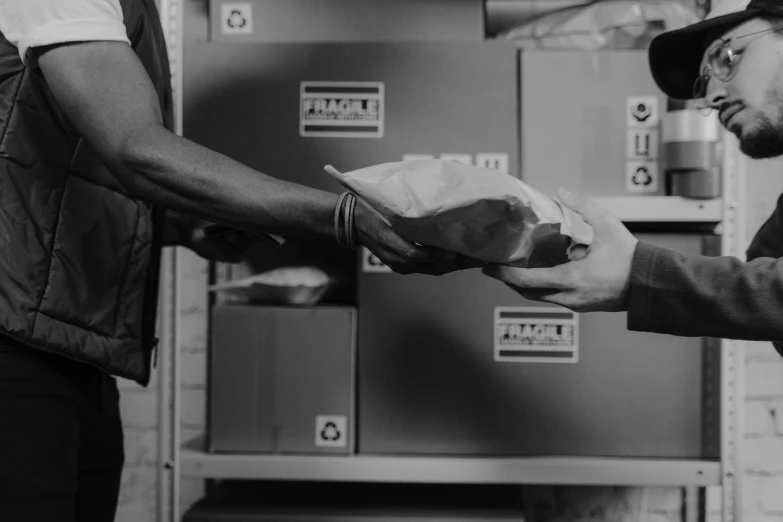 a man handing something to another man in a warehouse, a black and white photo, by Daniel Lieske, pexels contest winner, postage, 🌸 🌼 💮, in plastic, avatar image