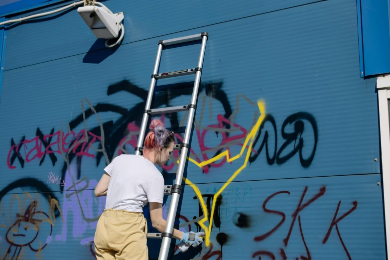 a woman is painting graffiti on the side of a building, by karlkka, pexels, ladders, avatar image