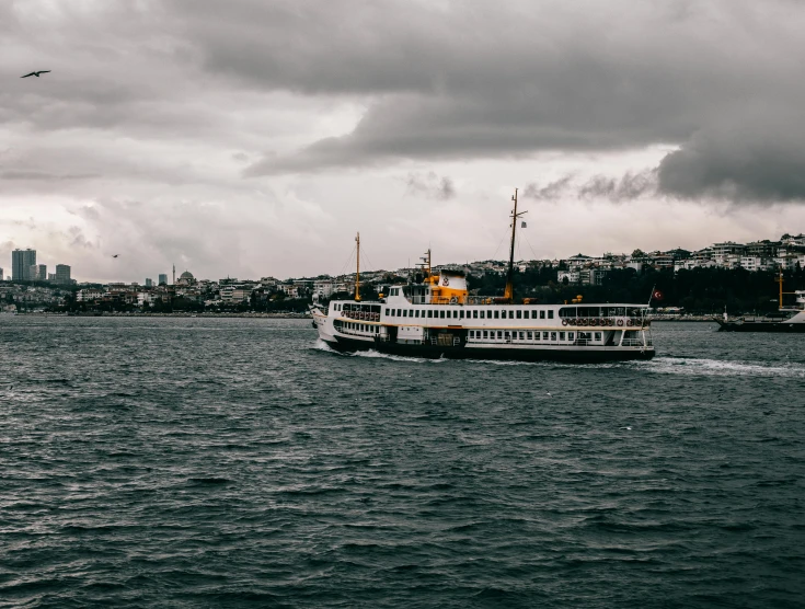 a boat on a body of water with a city in the background, by irakli nadar, pexels contest winner, hurufiyya, grey cloudy skies, ship at sea, 🚿🗝📝, thumbnail