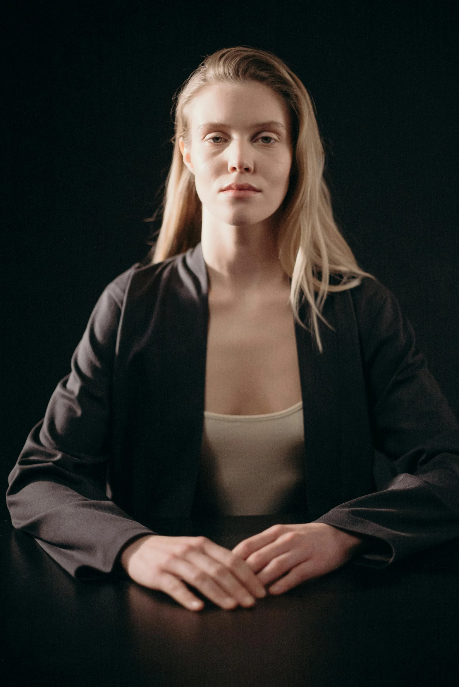 a woman sitting at a table in front of a black background, a character portrait, inspired by Louisa Matthíasdóttir, unsplash, open jacket, integrated synthetic android, wearing a black shirt, one model