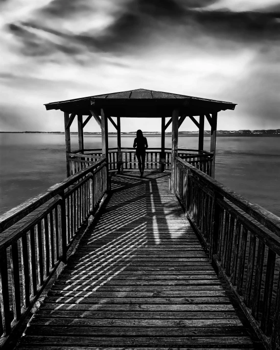 a black and white photo of a person on a pier, shrouded figure, wide angle landscape photography, photo pinterest, shutter