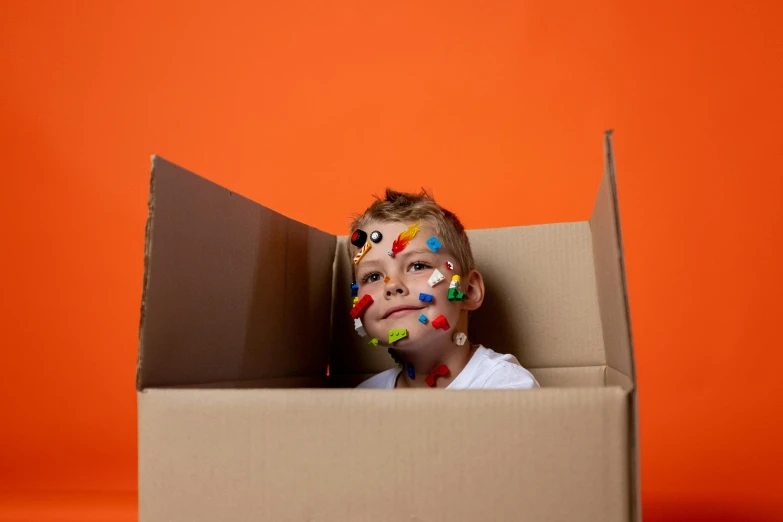 a young boy in a cardboard box with confetti sprinkles on his face, by Andries Stock, pexels, orange and cyan paint decals, square, gaming, toy commercial photo