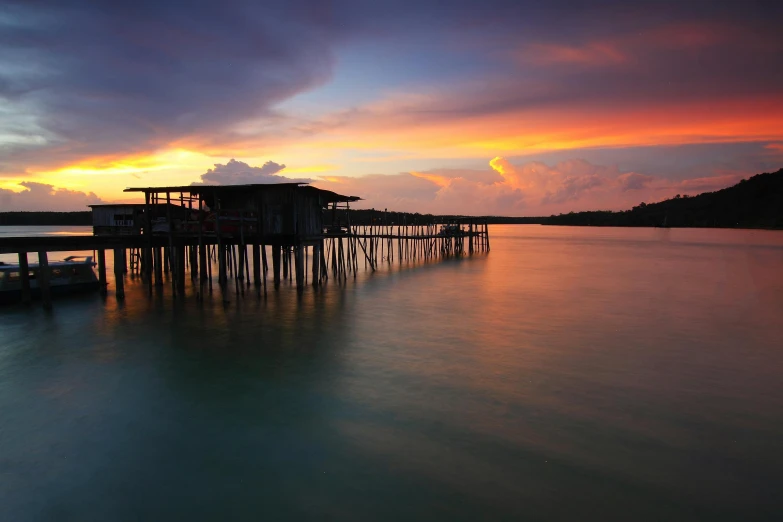 a boat sitting on top of a body of water, pexels contest winner, hurufiyya, houses on stilts, cloudy sunset, malaysian, intense colours