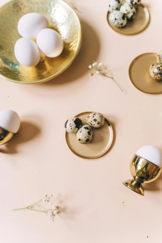 a bunch of eggs sitting on top of a table, a still life, by Lucette Barker, trending on unsplash, baroque, metallic brass accessories, sleek round shapes, adorable design, cups and balls