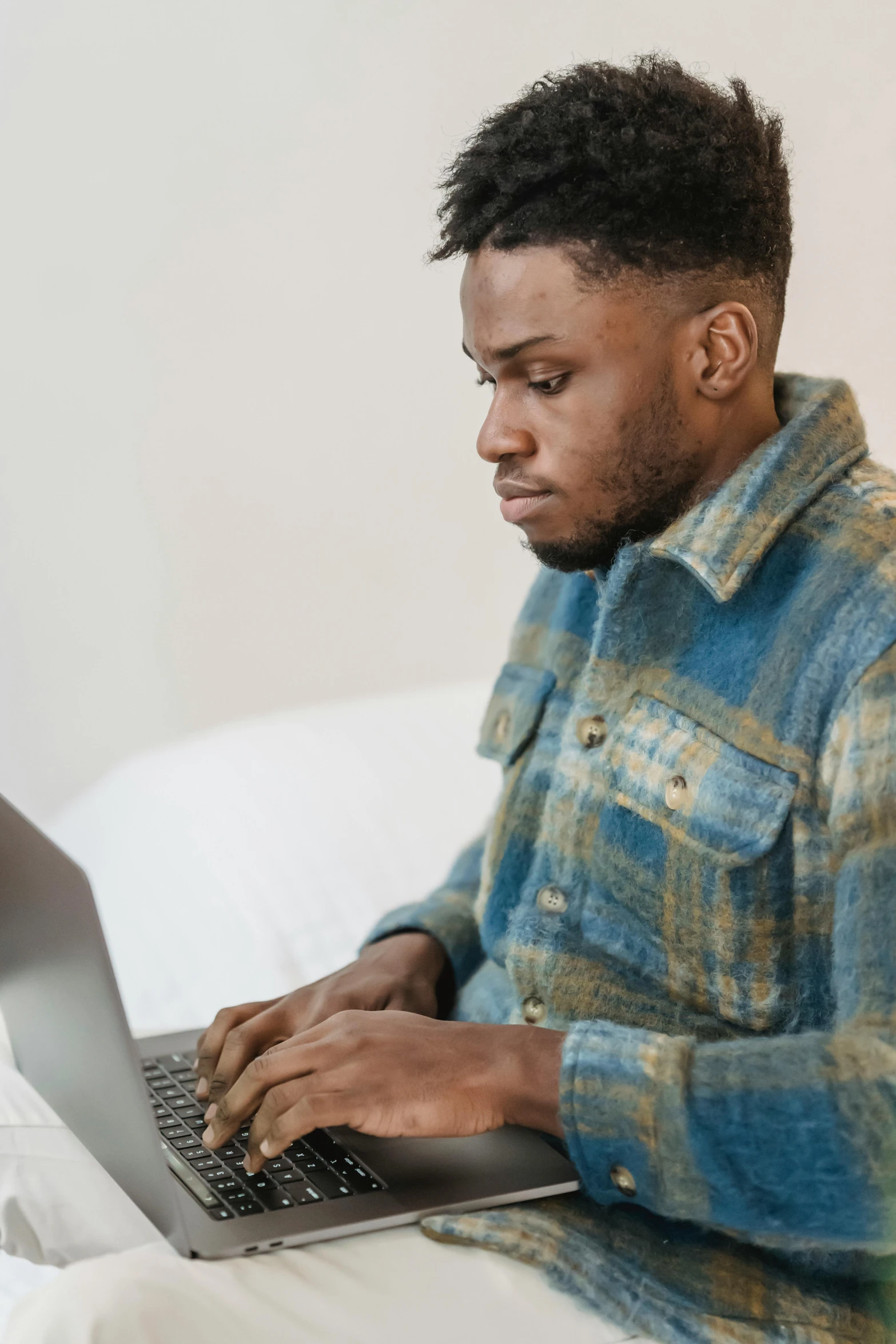 a man sitting on a bed using a laptop computer, trending on pexels, renaissance, man is with black skin, wearing a blue jacket, incompetent, wearing a flannel shirt