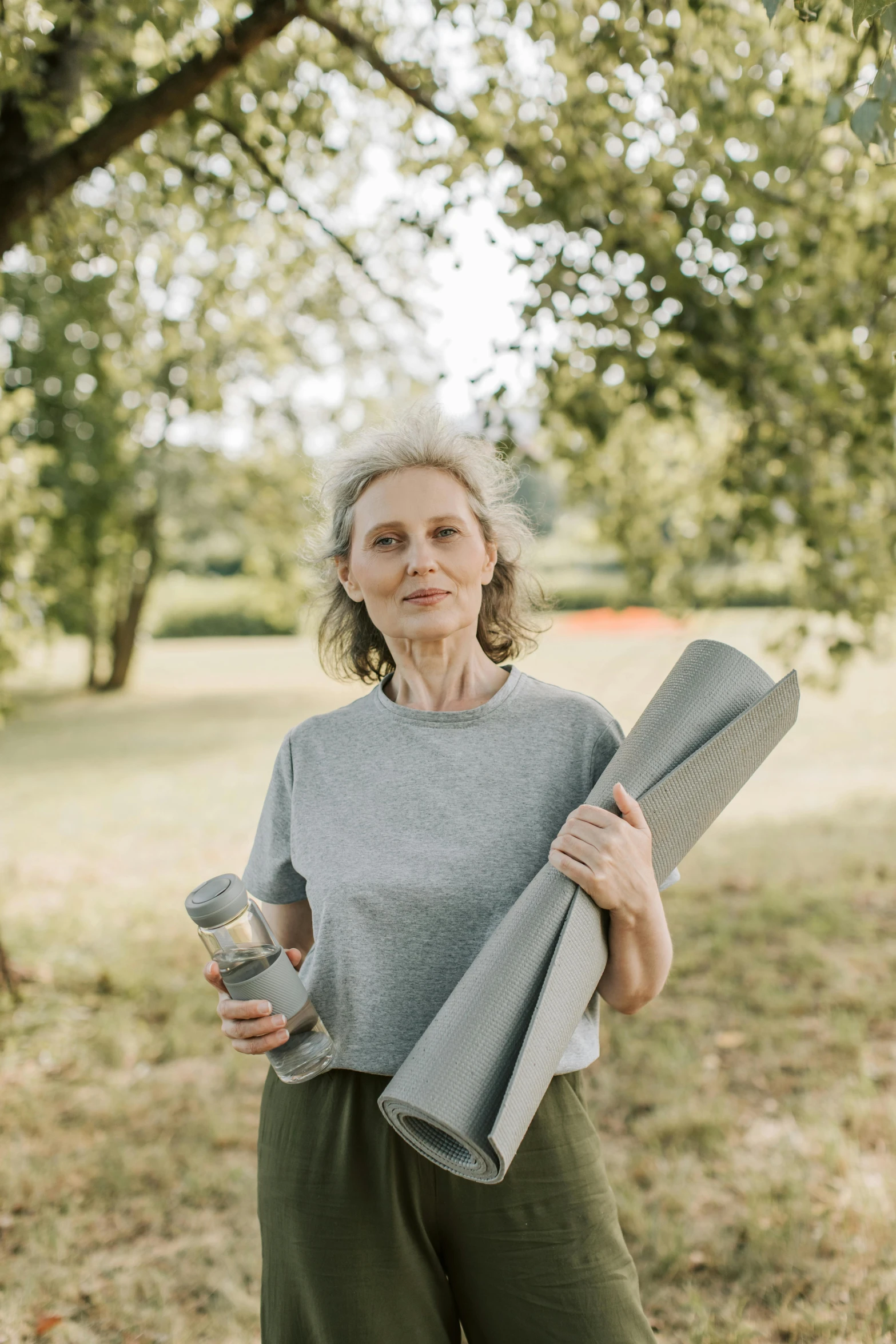 a woman holding a yoga mat in a park, a portrait, pexels contest winner, renaissance, aging, light grey, carrying survival gear, gray