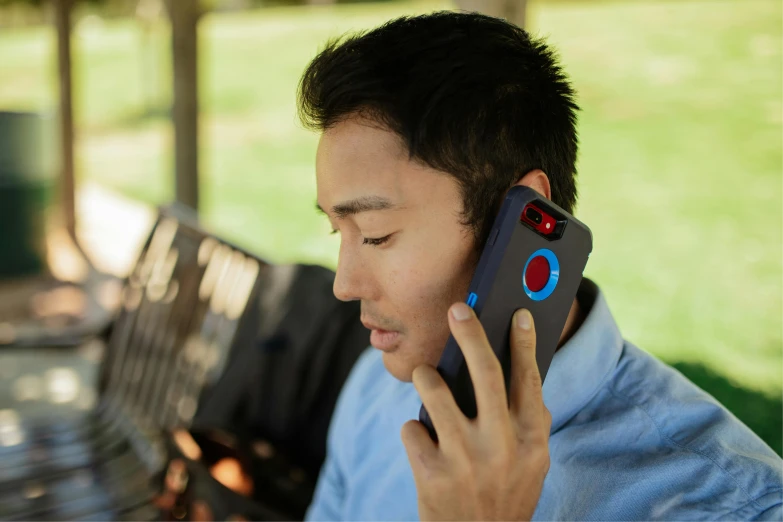 a man talking on a cell phone while sitting on a bench, blue and red two - tone, cell cover style, red dot, pictured from the shoulders up