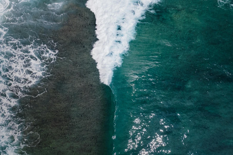 a person riding a surfboard on top of a wave, by Daniel Lieske, pexels contest winner, minimalism, coral reefs, close together, drone photograpghy, dark green water