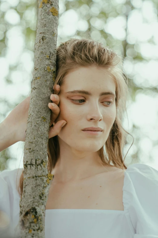 a woman in a white dress leaning against a tree, by Anna Boch, trending on pexels, romanticism, close up of face, at a fashion shoot, natural skin, dryad