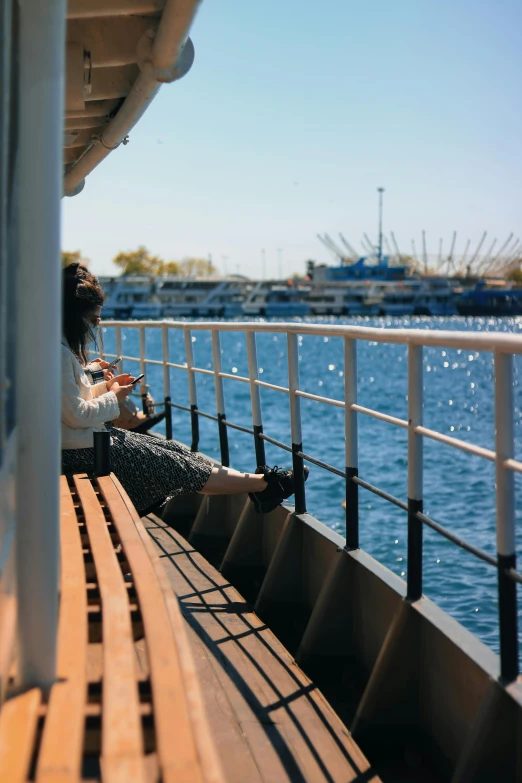 a woman sitting on a bench next to a body of water, on ship, rostov city, perfect crisp sunlight, sunday
