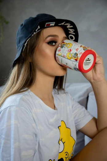 a woman sitting on a bed drinking out of a cup, a picture, trending on pexels, graffiti, red cap, anime girl drinks energy drink, official product image, cartoon paper coffee cup