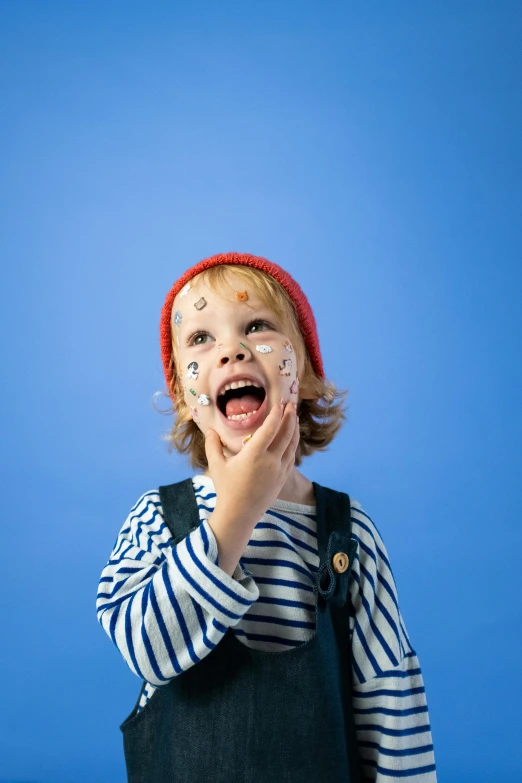 a little boy standing in front of a blue background, facepaint, french facial features, excited, breton cap