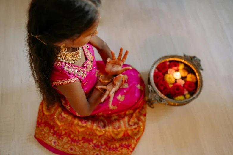 a little girl sitting on the floor next to a bowl of flowers, pexels contest winner, hurufiyya, hindu ornaments, glowing hands, hot pink and gold color scheme, holiday season