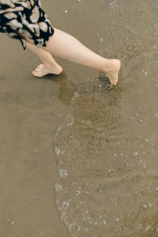 a woman standing on top of a sandy beach next to the ocean, inspired by Ruth Orkin, renaissance, detailed close foot shot, brown water, rectangle, minimalist