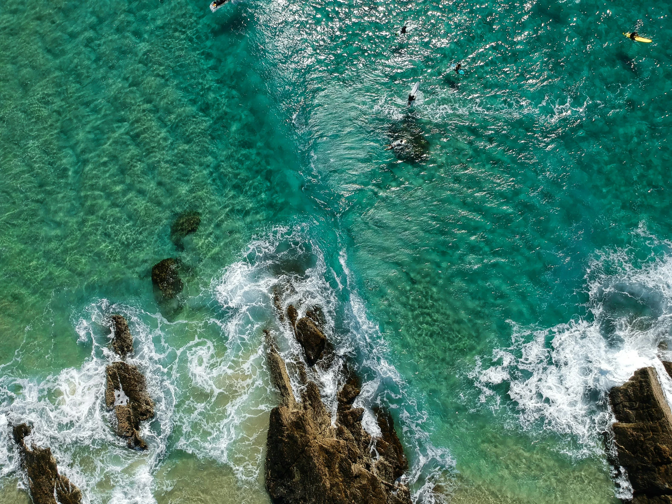 a group of people riding surfboards on top of a body of water, pexels contest winner, turquoise palette, rocky shore, helicopter view, high details photo