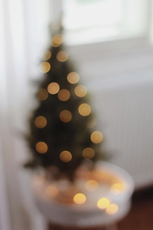 a small christmas tree sitting in front of a window, by Carey Morris, pexels, light and space, bokeh soft, backlighted, light haze, soft light - n 9