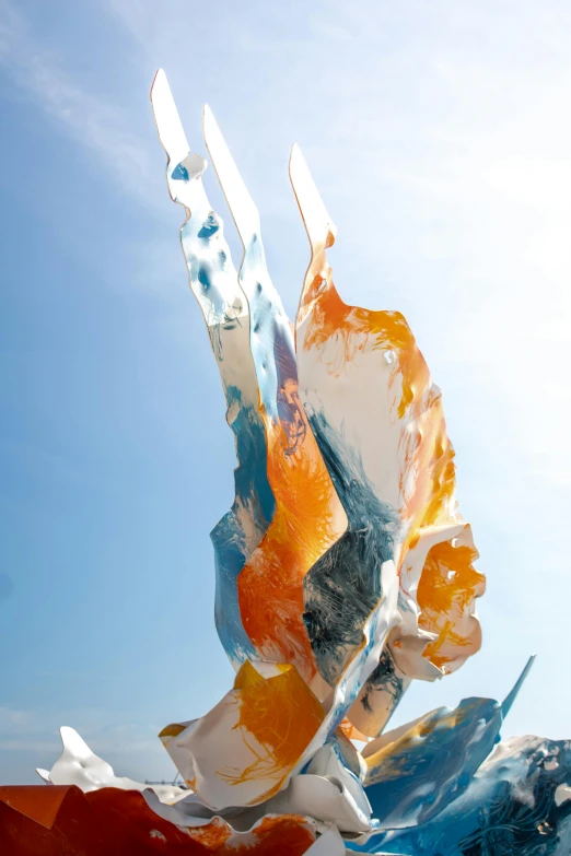 a sculpture sitting on top of a beach next to the ocean, an abstract sculpture, inspired by Lynda Benglis, unsplash, cyan and orange palette. vivid, translucent wings, face looking skyward, cast glass