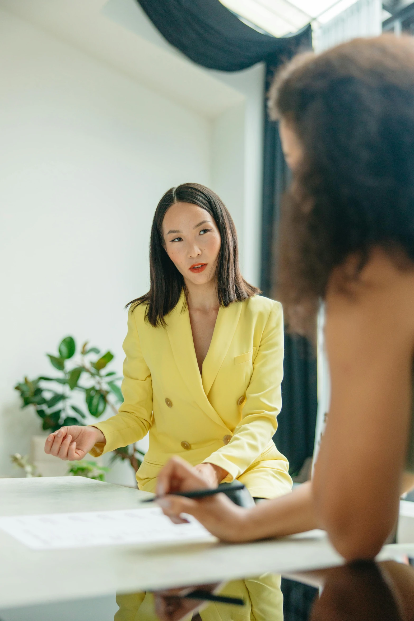 a woman in a yellow suit sitting at a table, trending on pexels, woman holding another woman, in a meeting room, asian descent, professional photo