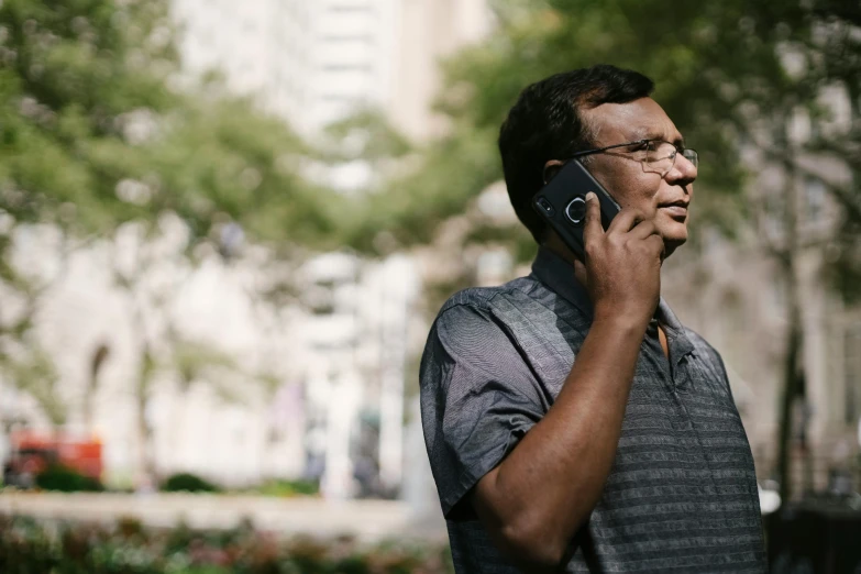 a man with glasses talking on a cell phone, by Dan Content, trending on unsplash, in a city park, diverse, ignant, ranjit ghosh