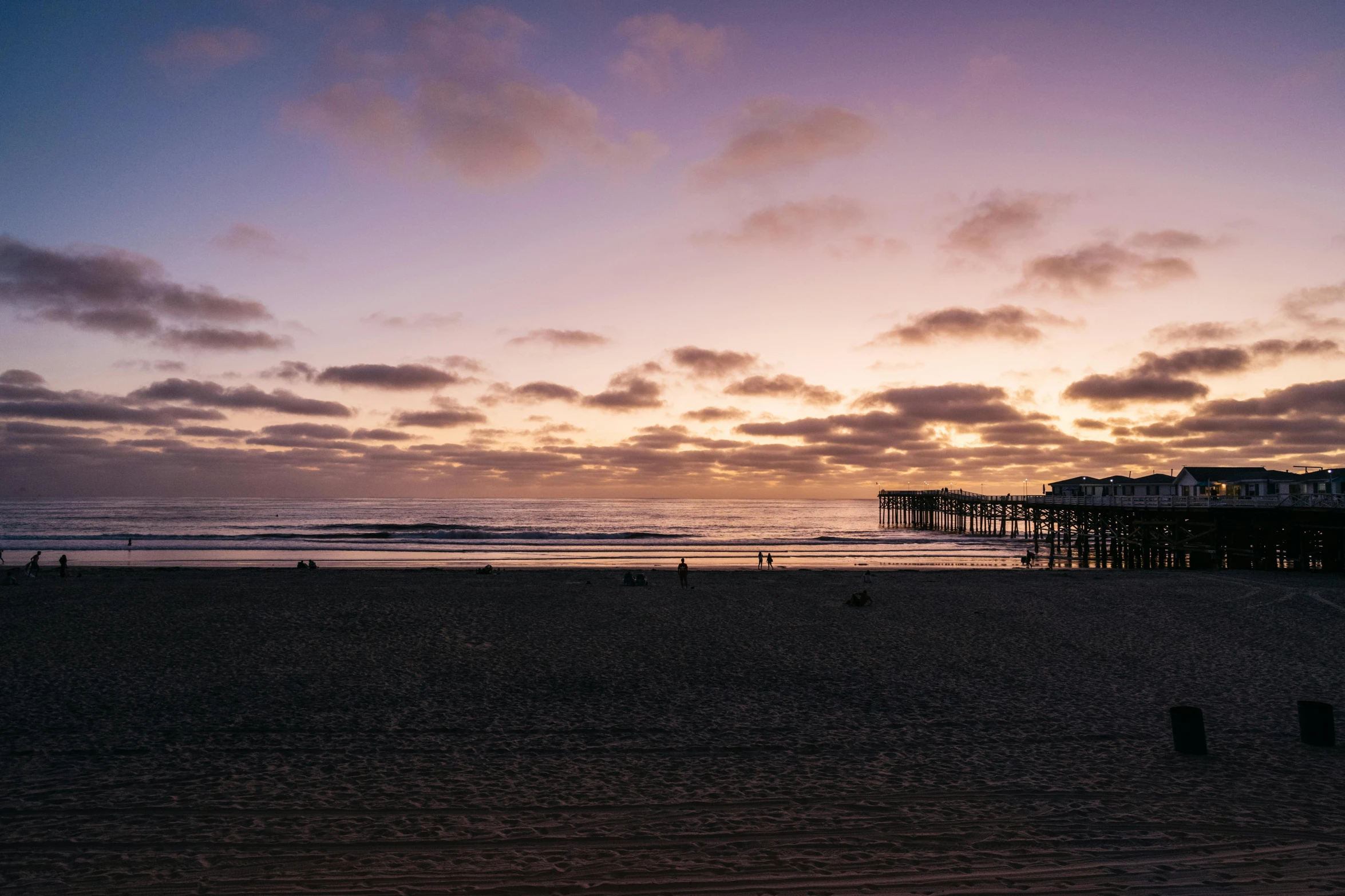 a group of people standing on top of a sandy beach, by Carey Morris, pexels contest winner, romanticism, sunset panorama, oceanside, on a cloudy day, a wooden