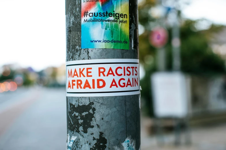 a sticker on a pole reads make racists afraid again, a poster, by Jakob Gauermann, trending on pexels, colorful”, faded glow, mixed race, agfa akurit