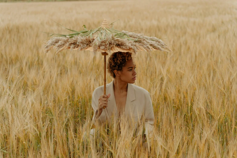 a woman standing in a field holding an umbrella, unsplash, renaissance, brown skinned, wearing hay coat, photoshoot for skincare brand, parasols