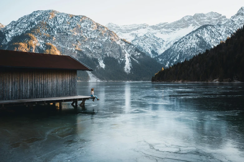 a boathouse sitting on top of a frozen lake, pexels contest winner, looking at the mountains, conde nast traveler photo, focus on full - body, muted colors. ue 5