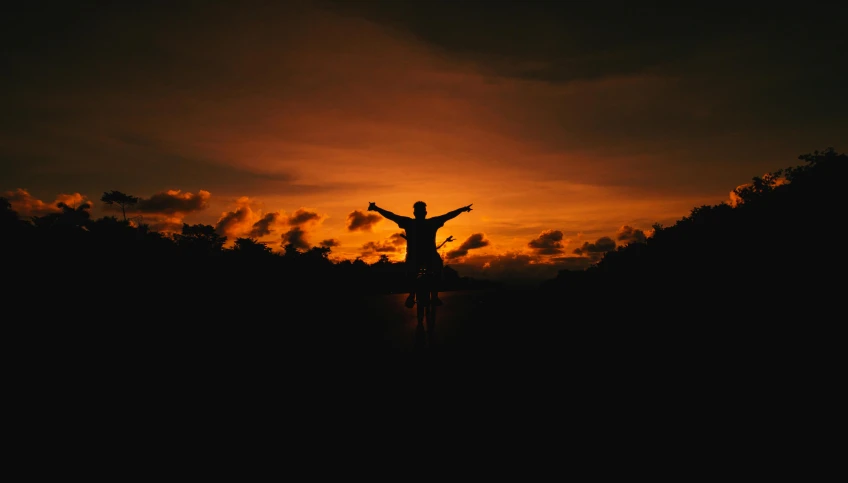 a silhouette of a person standing in front of a sunset, pexels contest winner, happening, pose(arms up + happy), avatar image, orange lit sky, dark setting